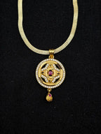 Gold necklace with a pendant featuring a red gemstone on a black background