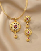 Gold necklace and earrings set with red gemstones on a beige fabric background