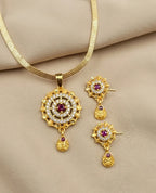 Gold necklace and earrings set with red gemstones on a beige fabric background