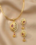 Gold necklace and earrings set with red gemstones on a beige fabric background