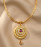 Gold necklace with a circular pendant featuring a red gemstone on a beige fabric background