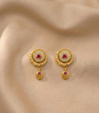 Gold earrings with red gemstones on a beige fabric background