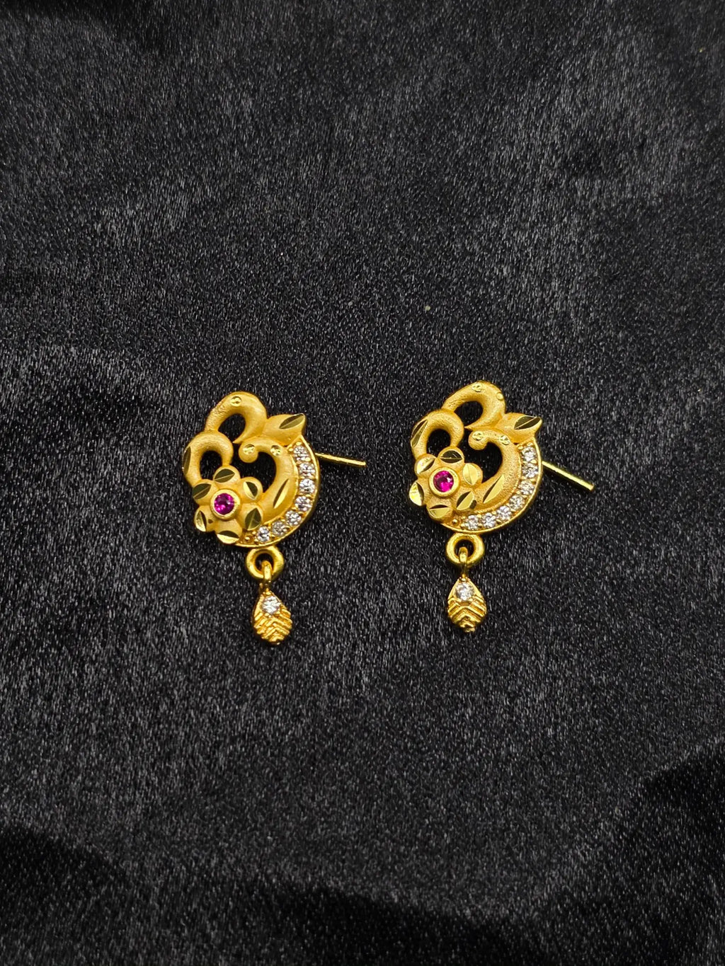Pair of gold earrings with floral design and red gemstones on a black background