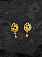 Pair of gold earrings with floral design and red gemstones on a black background