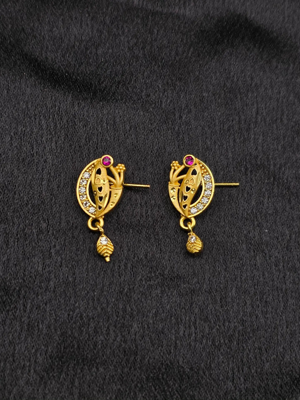 Pair of gold earrings with gemstones on a black fabric background
