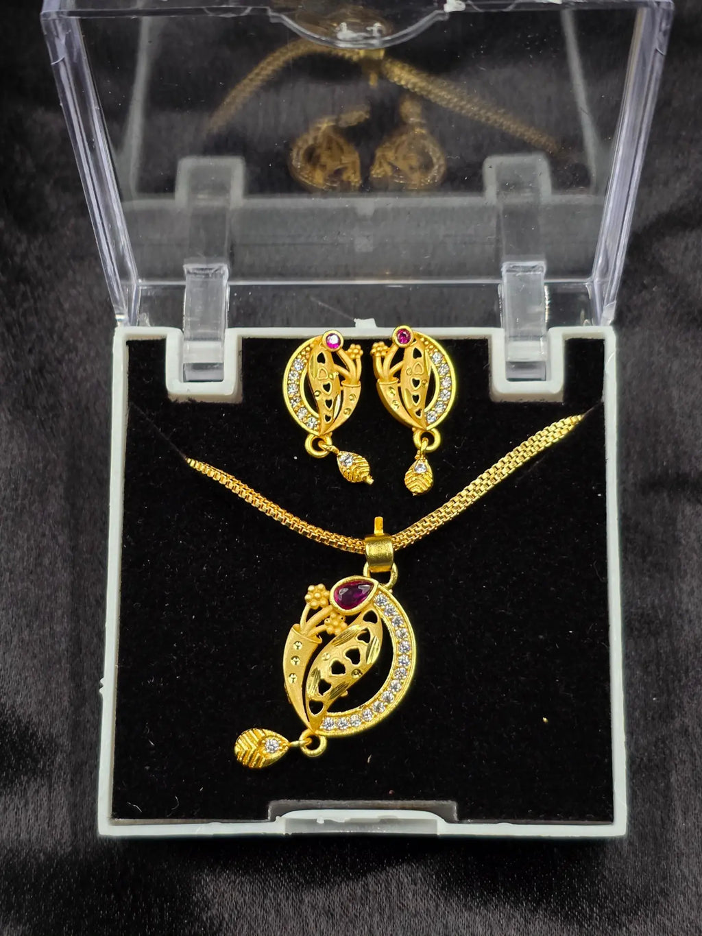 Gold jewelry set with necklace and earrings in a clear display case on a black background