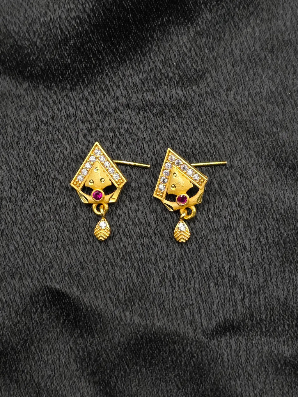 Gold earrings with gemstones on a black fabric background