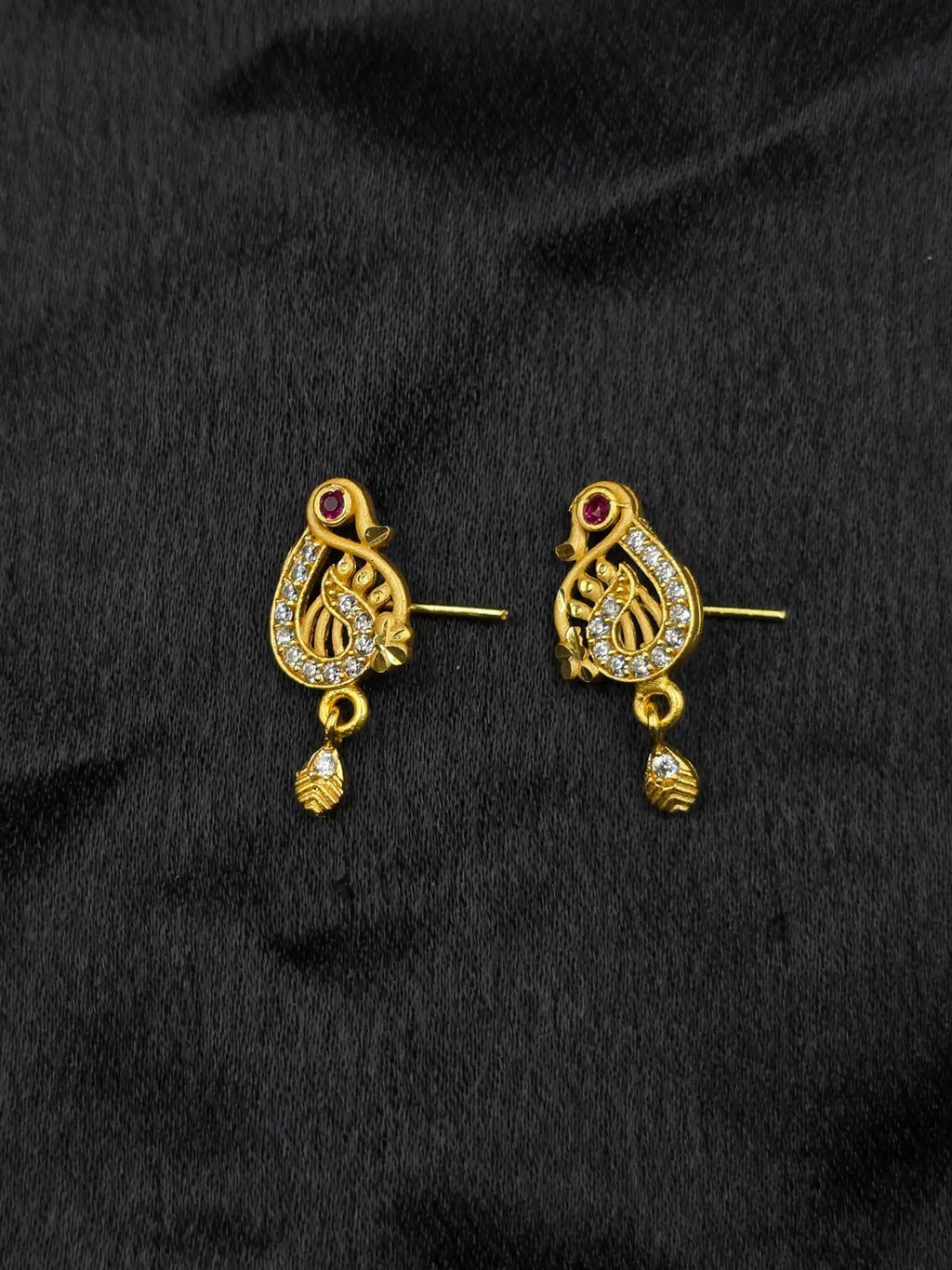 Pair of gold earrings with intricate designs on a black fabric background