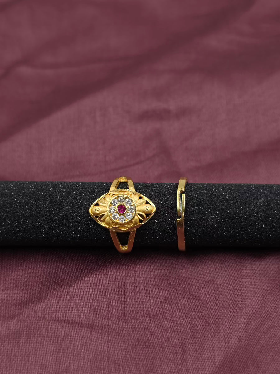 Gold ring with a red gemstone on a black rod against a maroon fabric background
