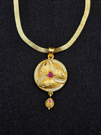 Gold necklace with a circular pendant featuring a red gemstone on a black background