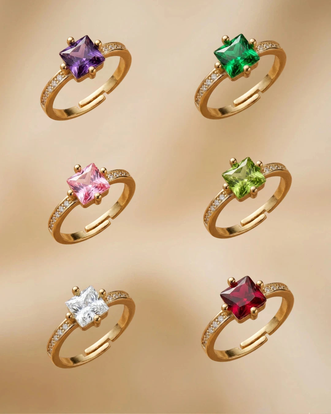 Set of six gold rings with colorful gemstones on a beige background