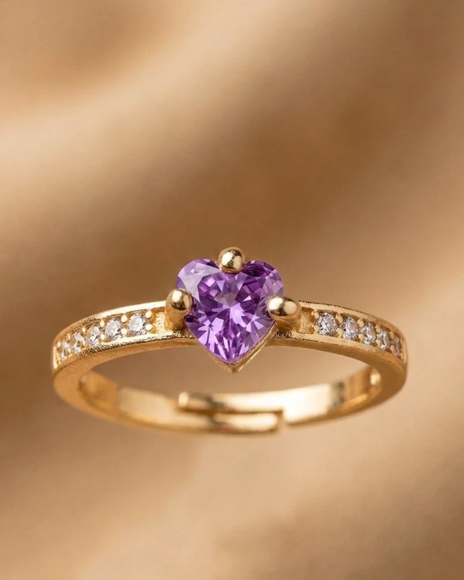 Gold ring with a heart-shaped purple gemstone on a gold background