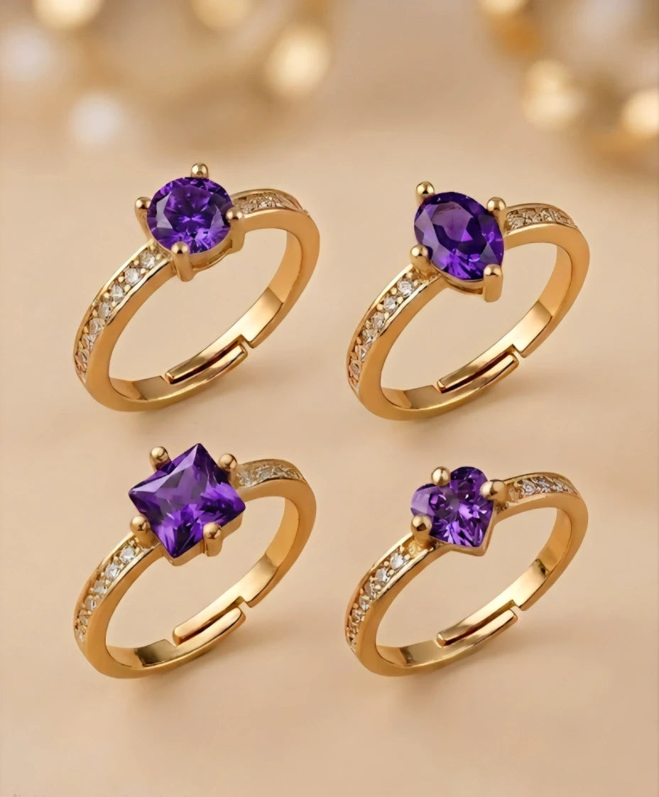 Four gold rings with purple gemstones on a beige background