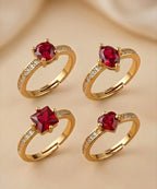 Four gold rings with red gemstones on a beige background