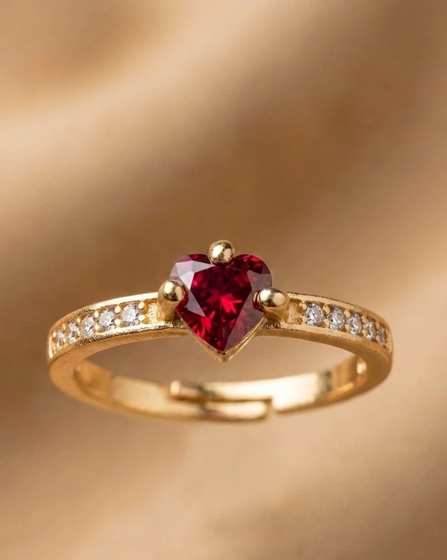 Gold ring with a heart-shaped red gemstone on a gold background