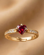 Gold ring with a heart-shaped red gemstone on a gold background